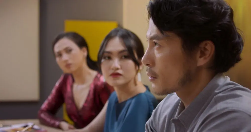 In SaiGon trong cơn mưa, a man sits with two women, all looking thoughtful in a gathering scene.