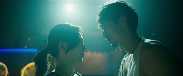 In the movie Mai, a man and a woman are facing each other under a green light, creating a tender moment.